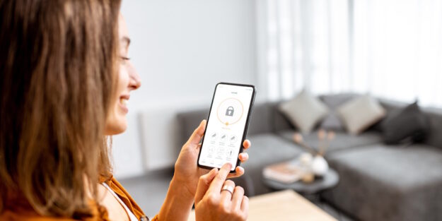 woman in her living room smiling and looking at a smart technology app on her phone woman in her living room smiling and looking at a smart technology app on her phone