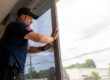 An Energy Solutions Window Tinting employee applies window film to a storefront window, using a squeegee to ensure a smooth, bubble-free finish.
