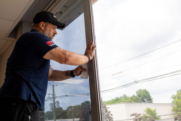 IMG_1960 An Energy Solutions Window Tinting employee applies window film to a storefront window, using a squeegee to ensure a smooth, bubble-free finish.