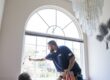An Energy Solutions Window Tinting employee carefully applies a layer of window film to a residential window, smoothing the film for a clean, precise finish.